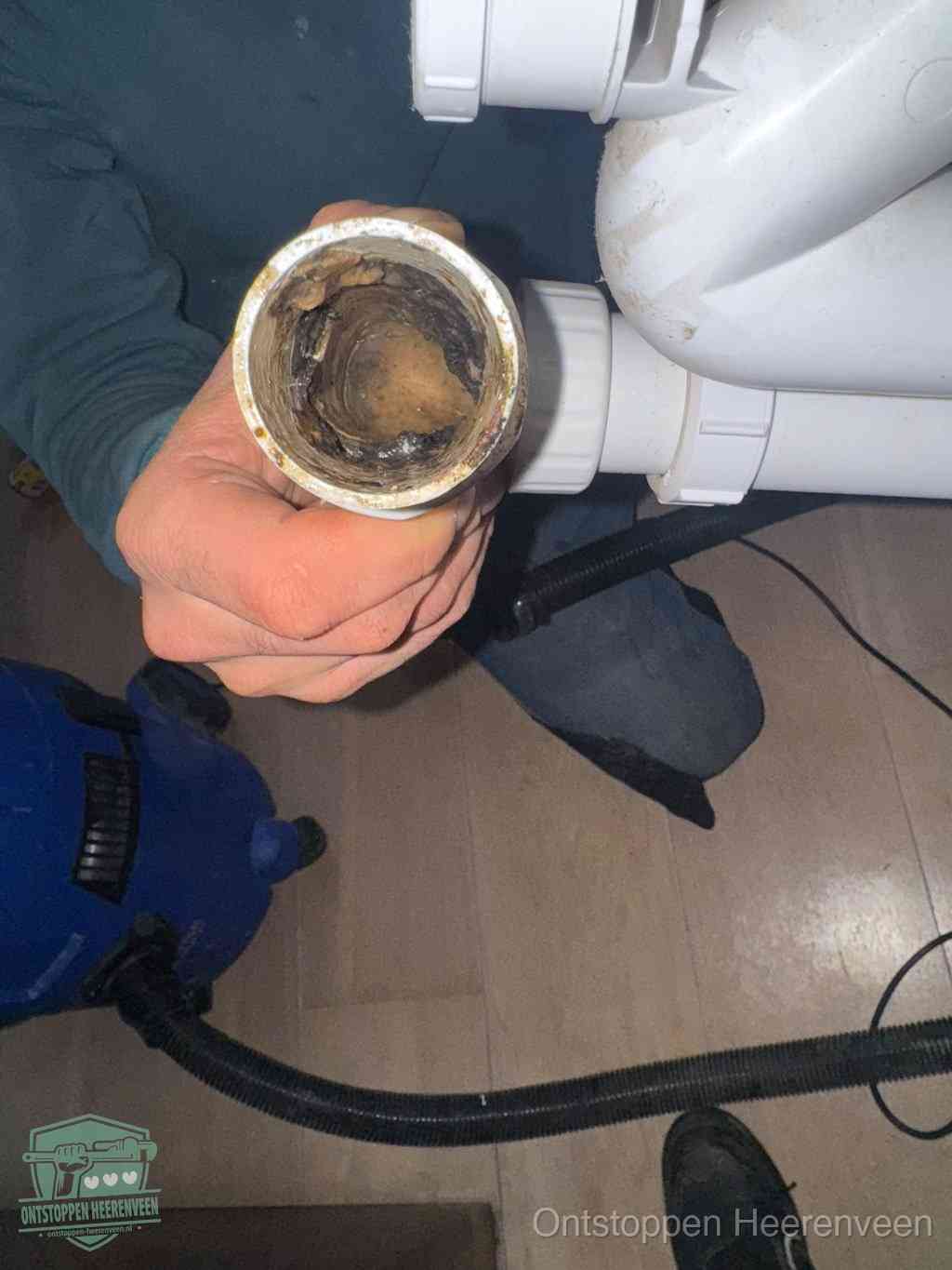Een hand houdt een losgekoppeld PVC-afvoerbuisstuk vast dat van binnen volledig is dichtgeslibd met vet, vuil en aanslag, de meest voorkomende oorzaak van een verstopte afvoer in Heerenveen