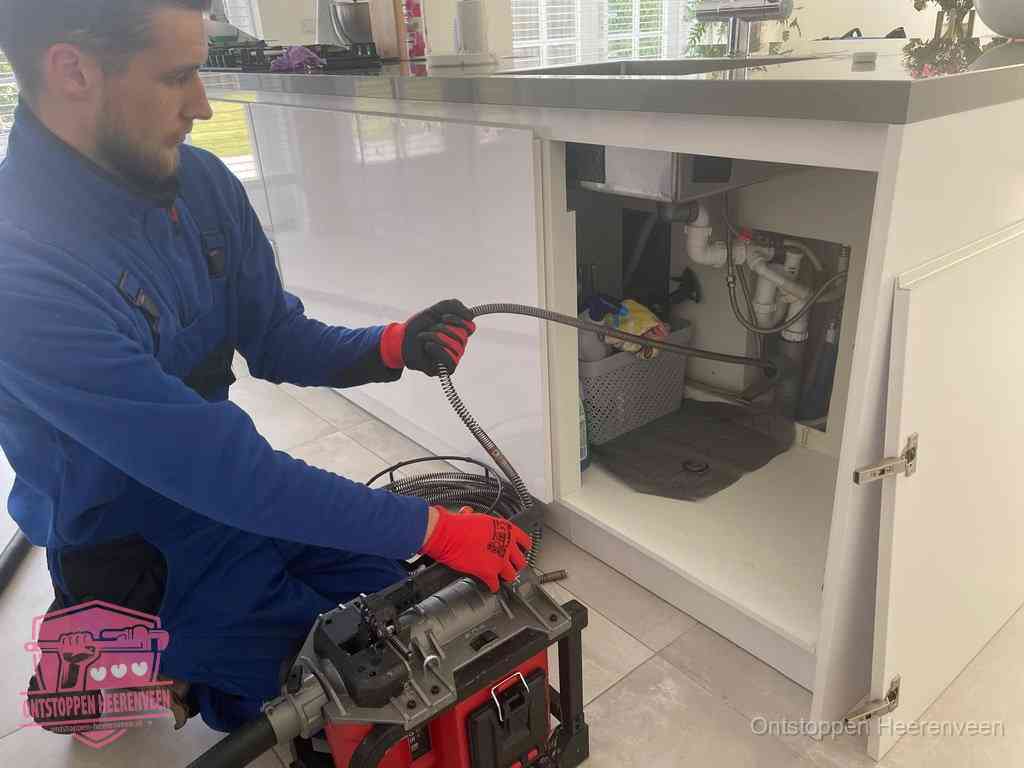 Monteur voert een ontstoppingsveer in de afvoer onder de keuken in Heerenveen