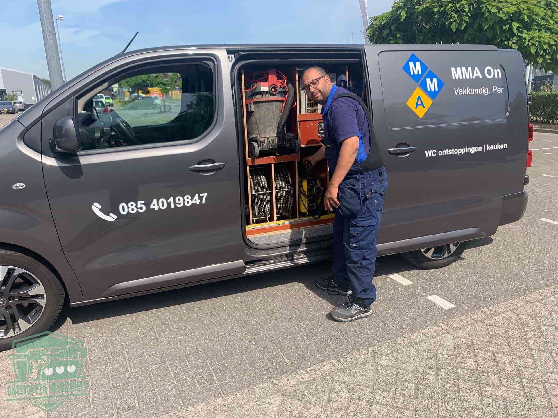 Een monteur bij de open schuifdeur van zijn bedrijfsbus op een parkeerplaats, klaar om de oorzaak van terugkerende afvoerverstoppingen aan te pakken in Heerenveen