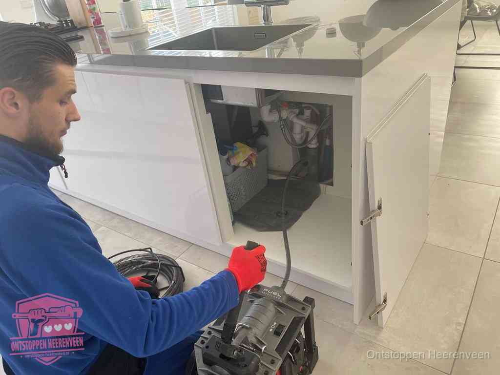 Monteur ontstopt met een veermachine een verstopte afvoer onder de gootsteen in Heerenveen