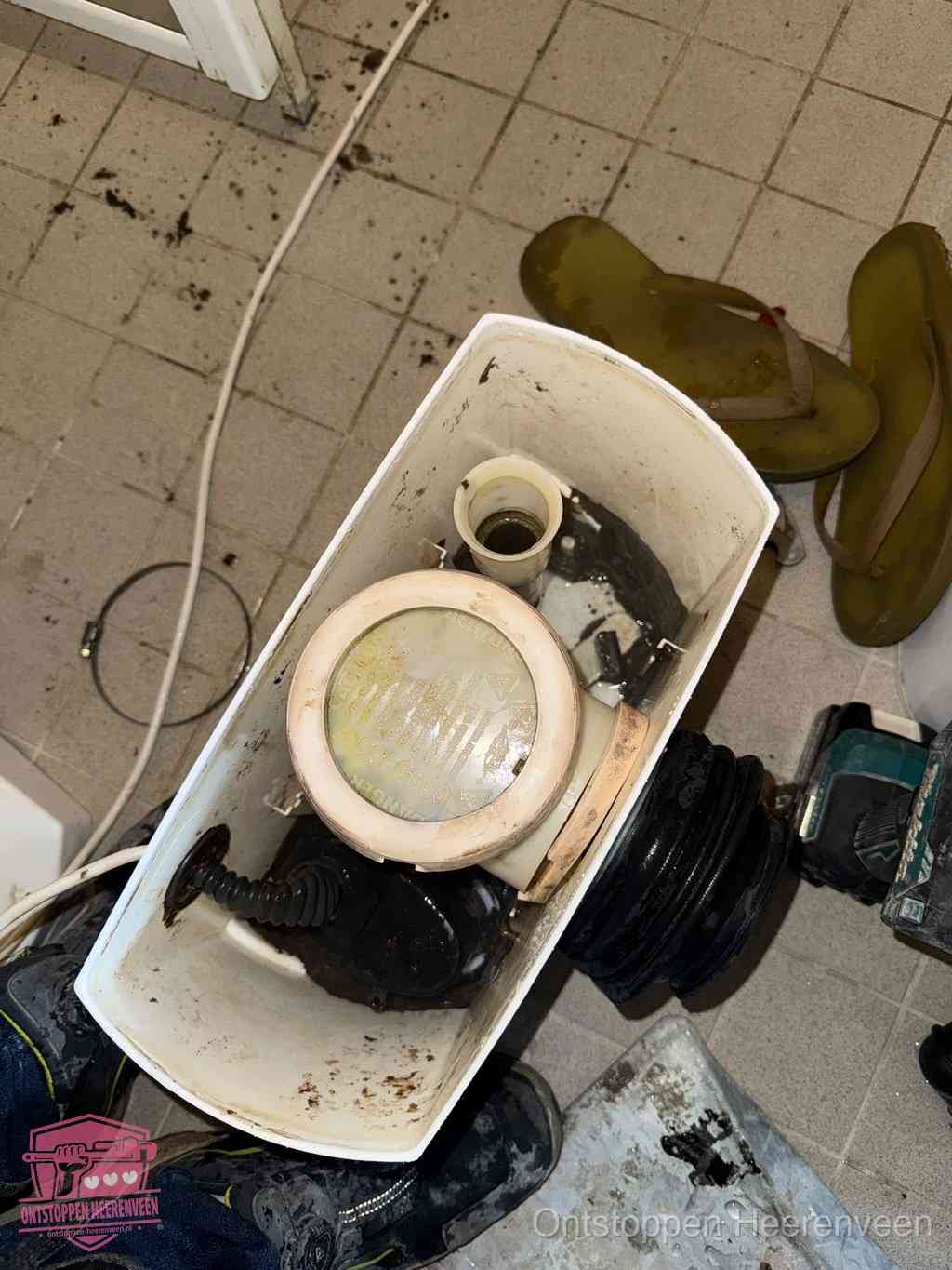 Een gedemonteerde toiletpot op de vloer met ontstoppingsveer en gereedschap ernaast, het verwijderen van een vastzittend voorwerp uit de wc in Heerenveen