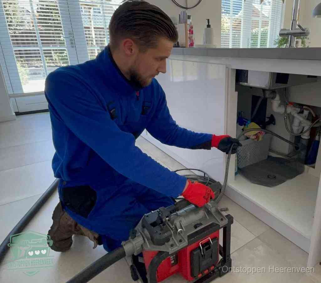 Een monteur met rode handschoenen knielt in een keuken en voert een elektrische ontstoppingsveer in tijdens het professioneel afvoer ontstoppen in Heerenveen