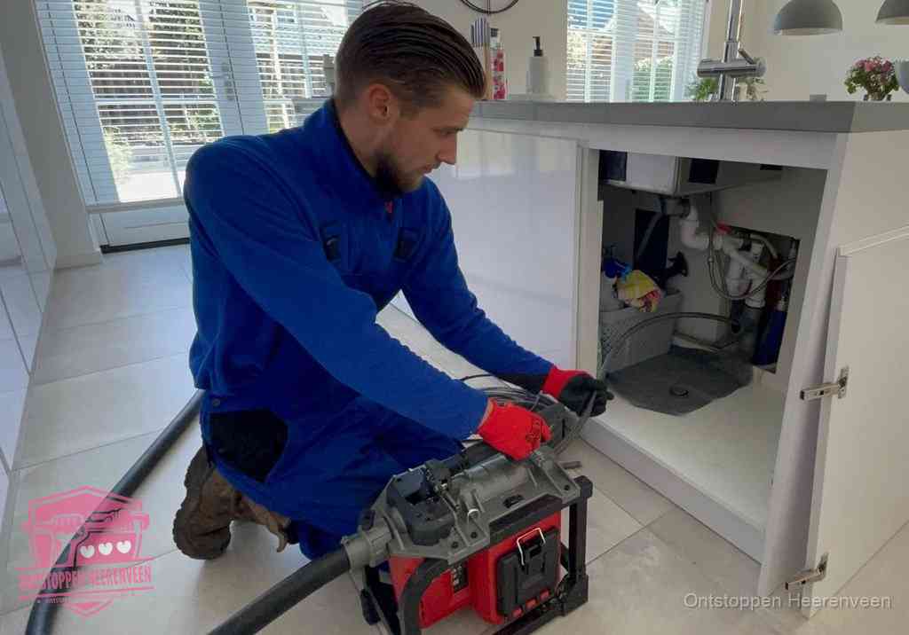 Een monteur voert een professionele elektrische ontstoppingsmachine in de afvoer onder de spoelbak tijdens het gootsteen ontstoppen in Heerenveen